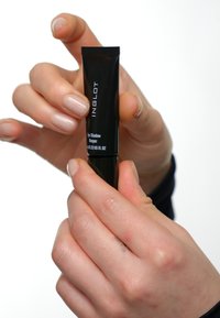 Svart tube med Inglot Eye Shadow Keeper holdt mellom fingrene, med hvit tekstetikett, glatt overflate og tapered dyse.