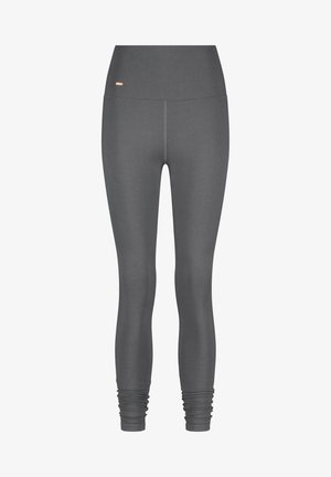 Harmaat legginsit, joissa on korkea vyötärö, saumaton muotoilu ja kerrottu nilkkadetaili. Vyötäröllä on pieni kultainen logo.