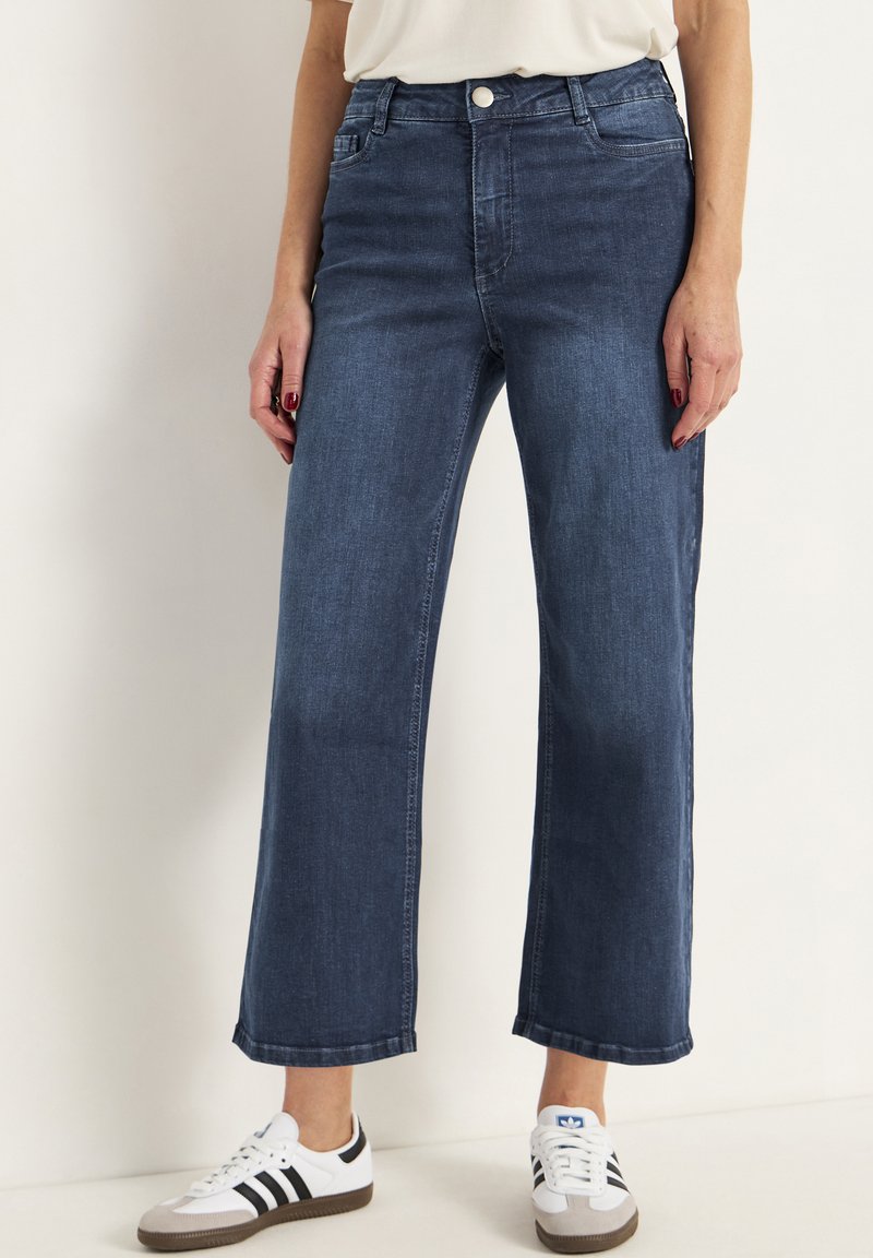 Tummansinisiä leveälahkeisia farkkuja, joissa on klassinen viiden taskun muotoilu, metallinen napitus ja puolistruktuurinen istuvuus.