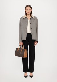 Manteau à carreaux gris et noir avec un col beige, porté sur un haut blanc et un pantalon noir. Tenant un sac à main à motif marron. Talons noirs.