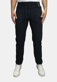 Navyblauwe broek met een comfortabele pasvorm, voorzien van een elastische tailleband, trekkoord en twee vo pockets. Draagt met witte sneakers.
