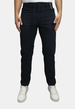 Navyblauwe broek met een comfortabele pasvorm, voorzien van een elastische tailleband, trekkoord en twee vo pockets. Draagt met witte sneakers.
