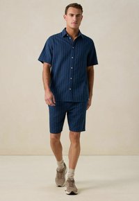 Blauwe gestreepte short-sleeve shirt en bijpassende shorts van een lichtgewicht stof. Draag met beige sneakers en sokken. Eenvoudige knopen op het shirt.