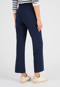 Marineblauwe op maat gemaakte broeken met een rechte pijp, voorzien van zijzakken en een gladde stoftextuur. G gedragen met beige en gouden sneakers.