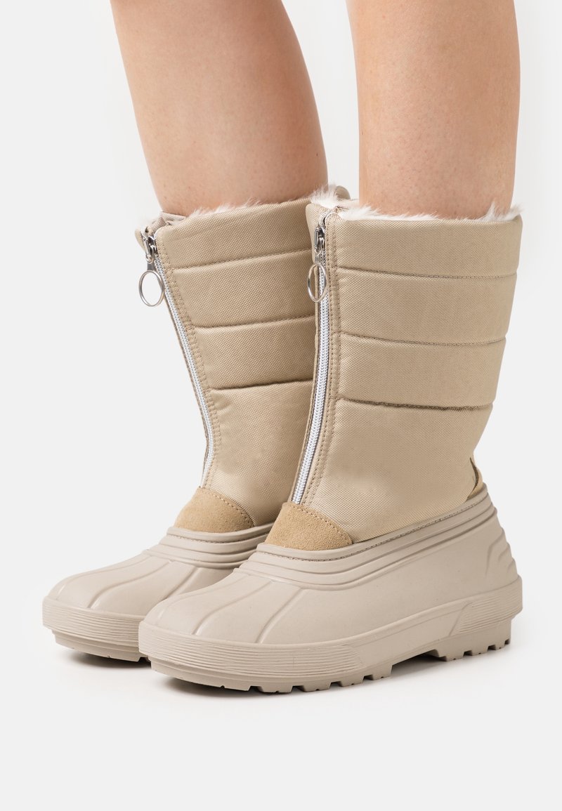 Botas de invierno beige con un cuello forrado de piel, parte superior de tejido acolchado y suela de goma con un agarre texturizado. Cierre de cremallera en la parte delantera.