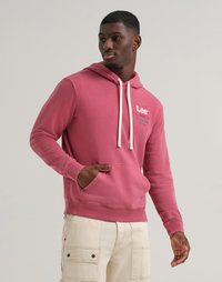 Felpa rosa con cappuccio e cordini, dotata di tasca frontale e dettaglio con logo, abbinata a pantaloni cargo di colore chiaro. Texture liscia.