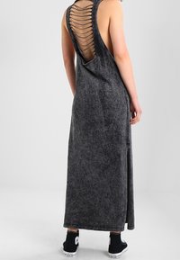 Osoba ubrana w bezrękawnikową, długą sukienkę w kolorze węgla, z plecami w stylu drabinki, połączoną z czarnymi trampkami za kostkę.