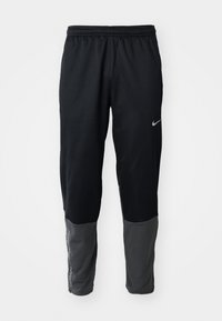 Czarne i ciemnoszare spodnie sportowe z elastycznym pasem i logo Nike na górnej lewej stronie uda oraz dolnej lewej nogawce.