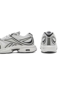 Para szarych i czarnych butów sportowych przedstawiona z widoku bocznego i tylnego na białym tle, podkreślająca detale wzornictwa i podeszwy.