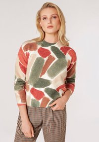 Maglione a maglia colorato e strutturato con motivi astratti in verde, rosso e beige, abbinato a pantaloni a scacchi. Collo rotondo, maniche lunghe.
