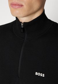 Black half-zip pullover made of knit material. Features a ribbed collar and a small white "BOSS" logo on the chest.