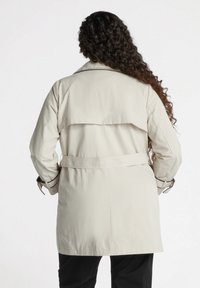 Beżowy trencz z paskiem w talii, długimi rękawami i tylnym klapą, wykonany z gładkiego materiału o eleganckim, minimalistycznym designie.