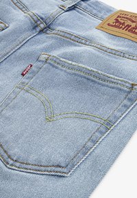 Heled sinise denimist teksad, millel on eristuv tagatasku kollase õmblusega, nahast silt brändingu jaoks ja punane sildikujundus.