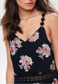 Kwiatowy top na ramiączkach w głębokim granacie z różowymi różami i koronkowymi detalami. Posiada wąskie ramiączka spaghetti z ozdobnymi akcentami.