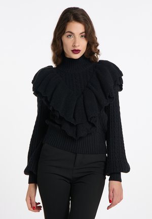 Schwarzer Strickpullover mit hohem Kragen und gestuften Rüschendetails. Verfügt über eine Zopfmusterstruktur und ausgestellte Ärmel. Getragen mit eng anliegenden schwarzen Hosen.