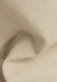 Beige tkanina s jemnou tkanou strukturou, zobrazená v detailním záběru s měkkými záhyby a jemnými stíny.