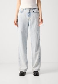 Jean taille haute bleu clair avec une coupe décontractée, présentant un léger délavage, cinq poches et des coutures contrastées le long des coutures.