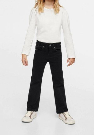 Jean en denim noir à coupe droite, cinq poches et fermeture par bouton, porté avec une chemise blanche à manches longues et des baskets claires.