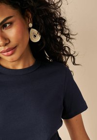 Navyblauwe katoenen T-shirt met een ronde halslijn, gecombineerd met grote, ingewikkelde, ivoorkleurige en gouden druppeloorbellen met kralen details.