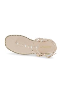 Sandal flat con design a strisce in beige chiaro e dettagli metallici. Presenta una soletta testurizzata e borchie decorative lungo i bordi.