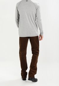 Grå långärmad skjorta, bruna kordflöjelbyxor, svarta skor. Synliga sömdetaljer. Skjortan har en raglanärmsdesign.