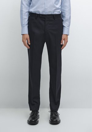 Navy dress pants with front pleats, a smooth texture, and a slim fit. Worn with a light blue striped shirt and black lace-up shoes.