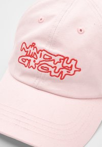 Casquette de baseball rose en coton doux. Présente un texte rouge brodé dans une police ondulée. Comprend des trous de ventilation et des détails cousus.