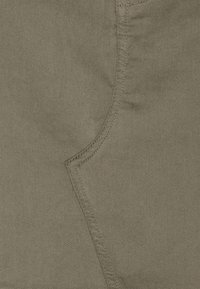 Tissu de couleur beige avec une texture lisse et des détails de couture bien visibles. Le matériau est durable avec un léger éclat et une légère élasticité.