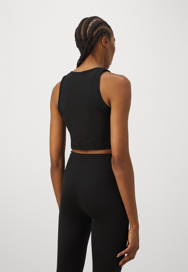 Un crop top de sport noir avec des bretelles réglables et une bande de logo texturée, associé à un legging noir taille haute, offrant une finition lisse.