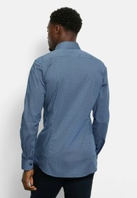 Blaue Langarmshirt mit geometrischem Muster, ausgestattet mit einem Button-Down-Kragen und strukturiertem Stoff. Die Rückansicht zeigt eine schmale Passform und einen abgerundeten Saum.