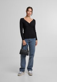 Pulover negru cu dungi ridicate, cu decolteu în V și detaliu răsucit, asortat cu blugi albastru deschis, adidași gri și o geantă mică neagră.