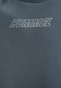 Grå atletisk skjorte med en tekstureret stofkvalitet og et fremtrædende hvidt "HUMMEL" logo på brystet.