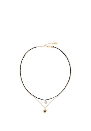 Collar de doble capa con una cadena negra de cuentas que sostiene una pequeña perla y una cadena dorada con un colgante de corazón dorado con un centro negro.