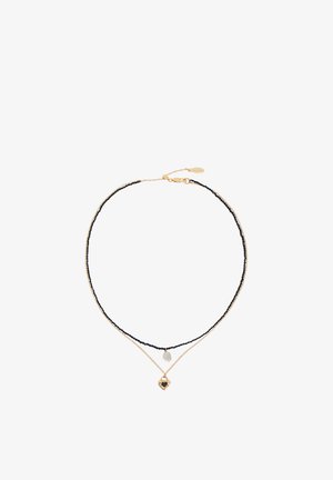 Dvoslojna ogrlica z eno črno ogrlico iz perlic, ki nosi majhno pero, in eno zlato verižico z zlatim obeskom v obliki srca s črnim središčem.