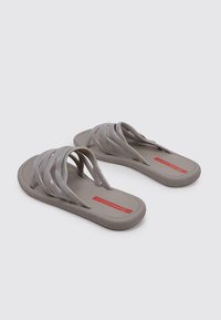 Chanclas grises con múltiples tiras superpuestas, una superficie texturizada y una suela sólida. Incluyen un detalle de logo rojo en la plantilla.