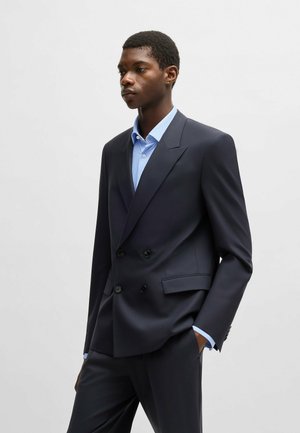 Giacca elegante navy a doppio petto con bottoni neri, abbinata a una camicia da uomo a scacchi blu chiaro, taglio sartoriale, tessuto morbido.