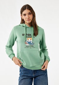 Felpa verde chiaro realizzata in tessuto morbido, con tasca frontale e un design grafico che presenta un personaggio dei cartoni animati, testo e vestibilità comoda.