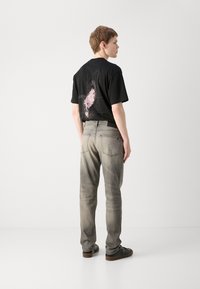 T-shirt nera in cotone con grafica e testo rosa sul retro, abbinata a jeans denim grigi chiari, indossata con scarpe nere.