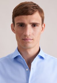 Camicia azzurra chiara con colletto realizzata in tessuto morbido, dotata di chiusura a bottoni e con una vestibilità leggermente rilassata e una consistenza soffice.