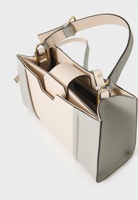 Grijze en crème handtas met een gestructureerde vorm, korrelige textuur, gouden hardware en een contrasterende binnenzak. Verstelbare schouderriem inbegrepen.