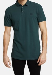 Groen poloshirt van gestructureerde stof, met een kraag, een drieknoopssluiting en een klein logo op de borst.