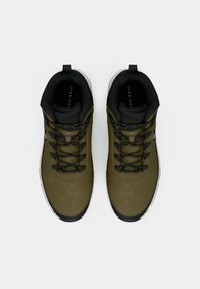 Grønne tursko med svarte detaljer, teksturert syntetisk overmateriale, runde lisser og en solid såle. Har en hælstropp for enkel påkledning.