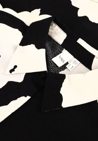 Zwart-witte gestreepte shirt met een puntkraag, gestructureerde stof en een waslabel zichtbaar nabij de nek.
