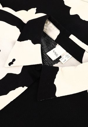 Zwart-witte gestreepte shirt met een puntkraag, gestructureerde stof en een waslabel zichtbaar nabij de nek.
