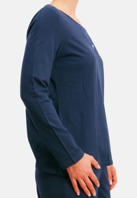 Marineblaues Langarmshirt aus weichem Stoff, mit V-Ausschnitt und schlichtem Design, verziert mit einem kleinen Emblem auf der linken Brustseite.