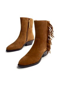 Botines de ante marrón con punta afilada, cremallera lateral con detalle de borlas y acentos de flecos en el lado exterior. Tacón bloque de altura media.