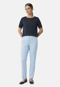 Marineblauw T-shirt met korte mouwen en ronde hals, gecombineerd met lichtblauwe tapered trousers en zwarte ballerina's, staande tegen een witte achtergrond.