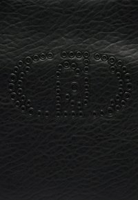 Superficie in pelle nera testurizzata impressa con borchie metalliche circolari che formano un logo "CBD" stilizzato al centro del telaio.