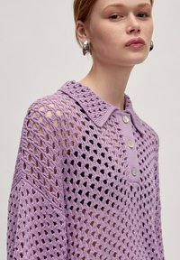 Lila gebreide poloshirt met een textuur van open gaas, een kraag en drie knoopsluitingen. Zacht, lichtgewicht stof.