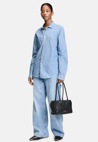 Hellblaues Denimhemd mit langen Ärmeln und zwei Brusttaschen, kombiniert mit weit geschnittenen hellblauen Jeans. Schwarze Lederhandtasche mit Schulterriemen.
